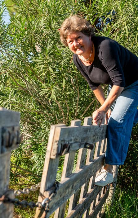 Renate Lorenz in Jeans und dunklem T-Shirt klettert über einen Zaun.